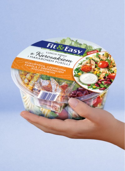 Opakowanie sałatki Fit&Easy z kurczakiem i makaronem trzymane na niebieskim tle.